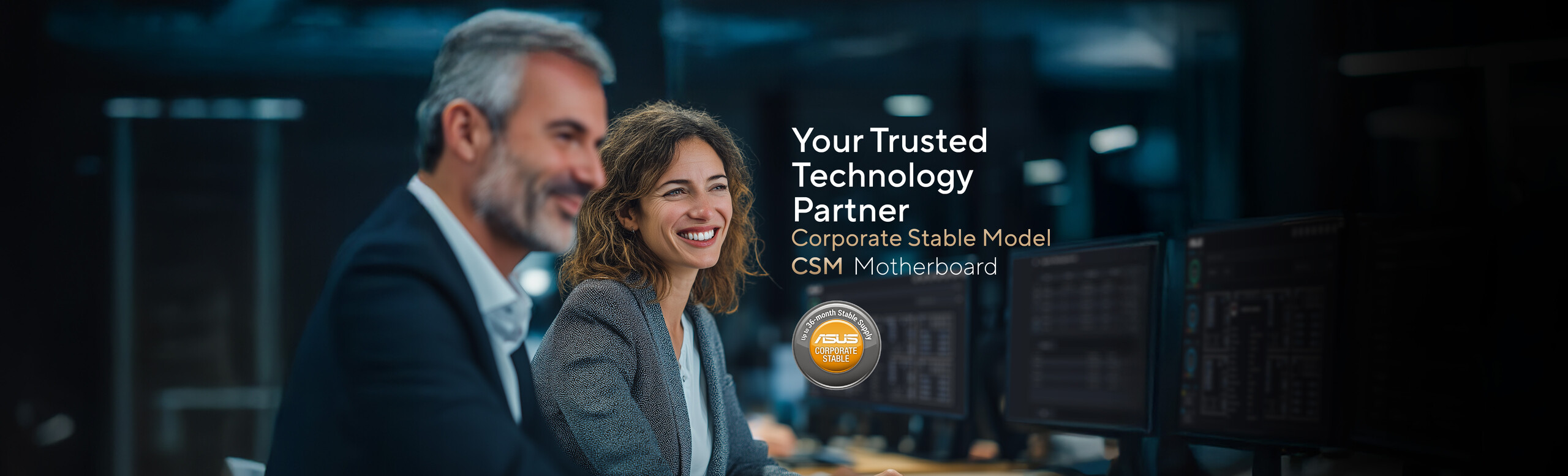 A man in a suit and a woman with wavy, light brown hair wearing a business jacket and white shirt are seated together at a desk in a modern office setting. Computer monitors are visible in the background, alongside promotional text for ASUS Corporate Stable Model (CSM) Motherboard: Your Trusted Technology Partner, and a circular badge stating 'Up to 36-month Stable Supply.'