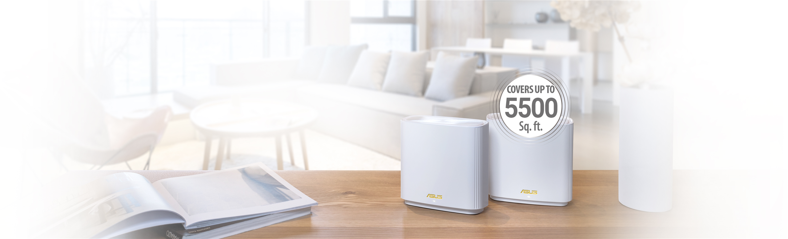 L'immagine mostra due nodi si un sistema mesh su un tavolo in un ambiente domestico. Sono di colore bianco e mostrano il marchio ASUS. Sopra di loro, c'è un'etichetta che indica COPRE FINO A 5500 sq. ft. Sullo sfondo si vede un salotto con un divano, un tavolino e un'atmosfera luminosa e moderna. Sul tavolo, accanto ai dispositivi, c'è un libro aperto.