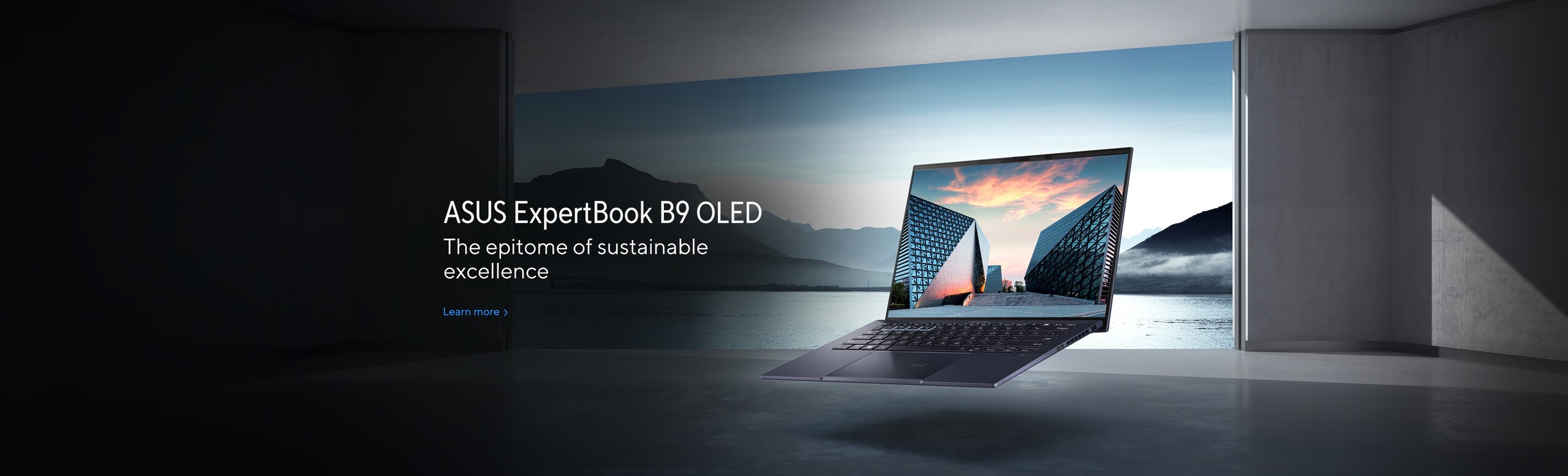 ASUS ExpertBook B9 OLED levitira u sivoj prostoriji kojoj se pruza pogled na more i planine, istaknut je njegov OLED ekran kao i njegov minimalisticki i tanak dizajn
