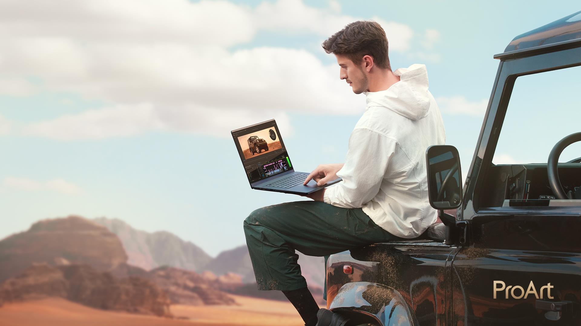 A man sitting on a truck in a desert using an ASUS laptop
